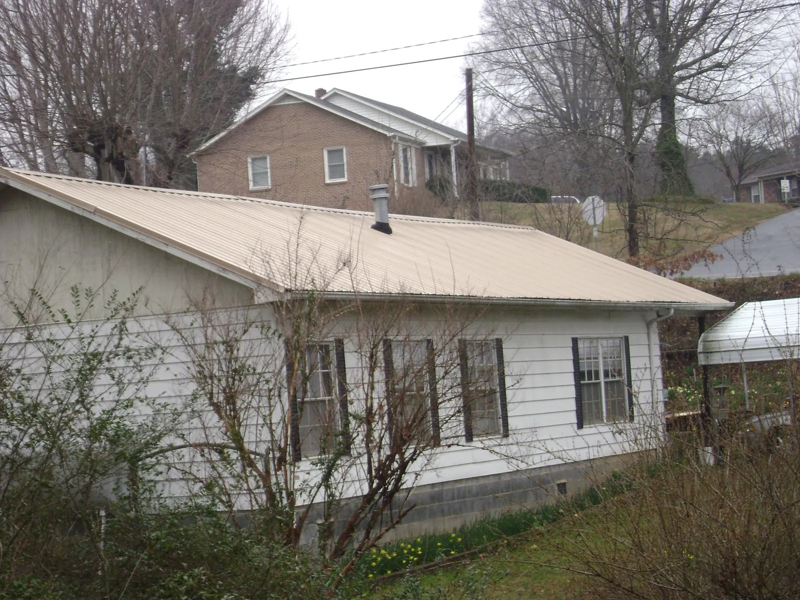 Tan metal roof on a white sided house set into a hillside — Commercial Roofing by Roofing Brothers in Killeen